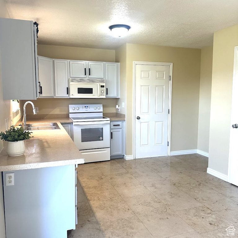 Kitchen featuring sink, a textured ceiling, light tile patterned flooring, and white appliances