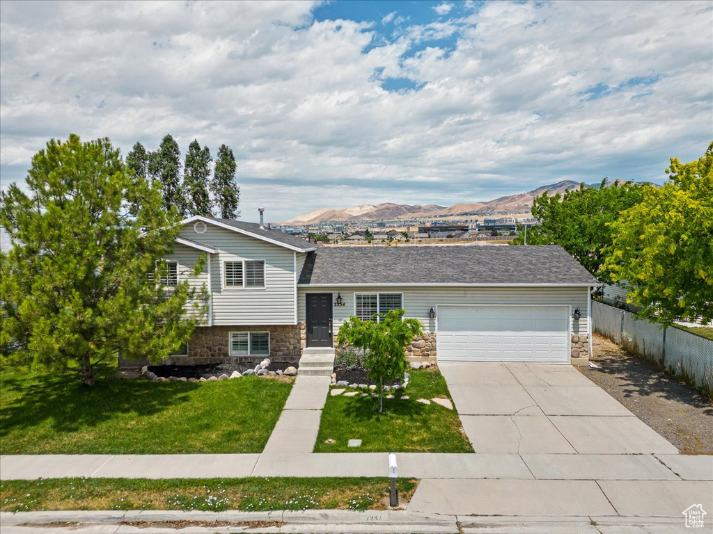 Split level home featuring a mountain view, a garage, and a front lawn