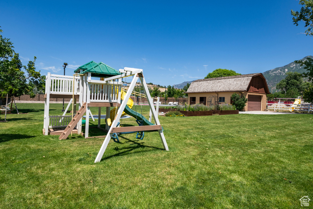 View of playground with a lawn, a mountain view, and an outdoor structure