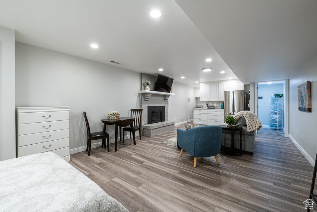 Bedroom featuring stainless steel fridge, wood-type flooring, and a brick fireplace