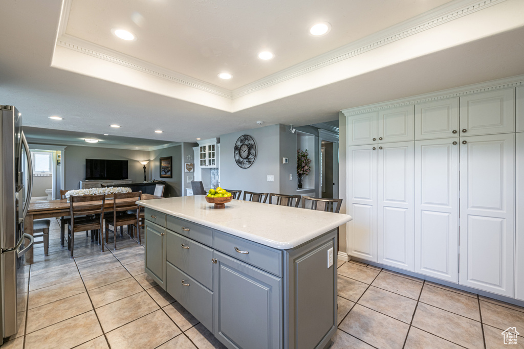 Kitchen with a tray ceiling, crown molding, a kitchen island, stainless steel fridge, and light tile patterned floors