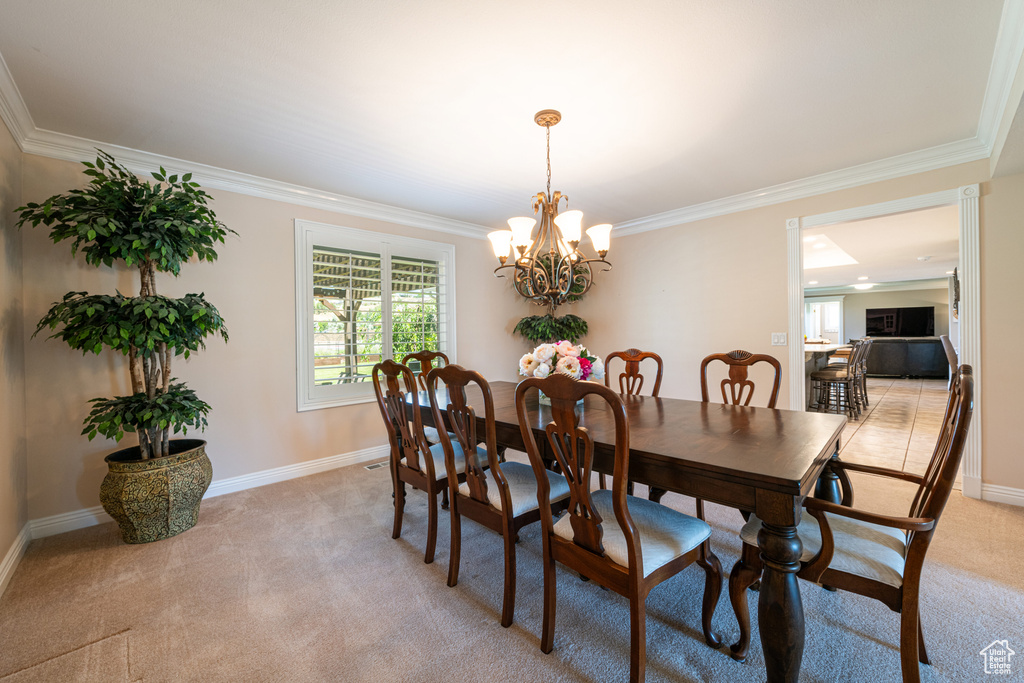 Dining area with ornamental molding, light colored carpet, and a chandelier