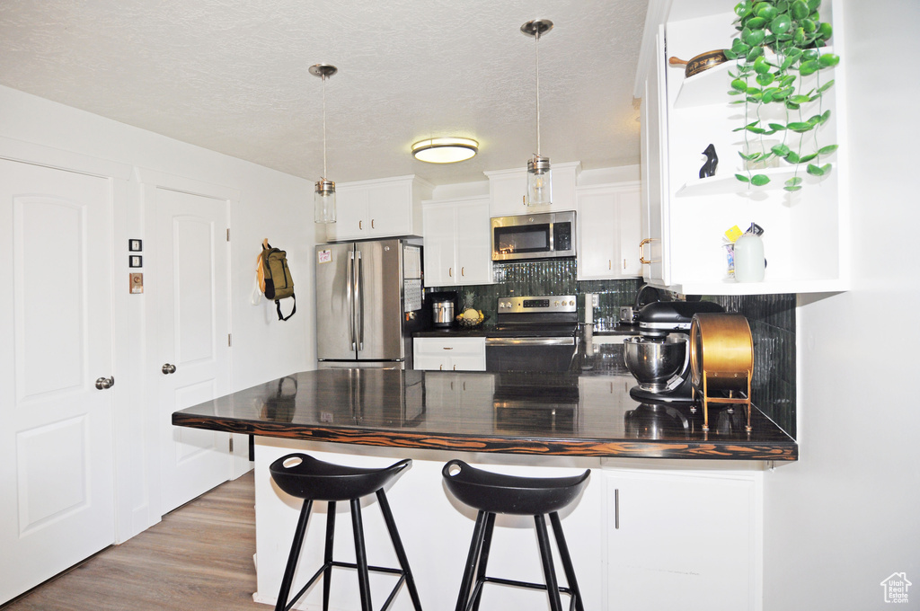 Kitchen featuring stainless steel appliances, white cabinets, pendant lighting, light hardwood / wood-style floors, and decorative backsplash