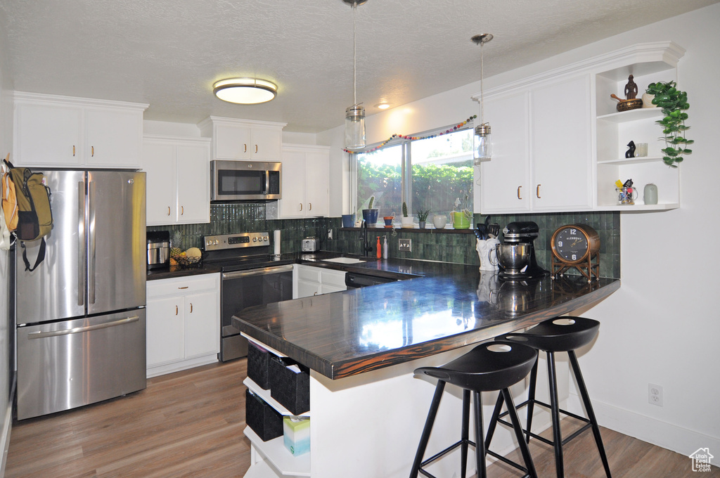 Kitchen with kitchen peninsula, backsplash, stainless steel appliances, hanging light fixtures, and hardwood / wood-style flooring