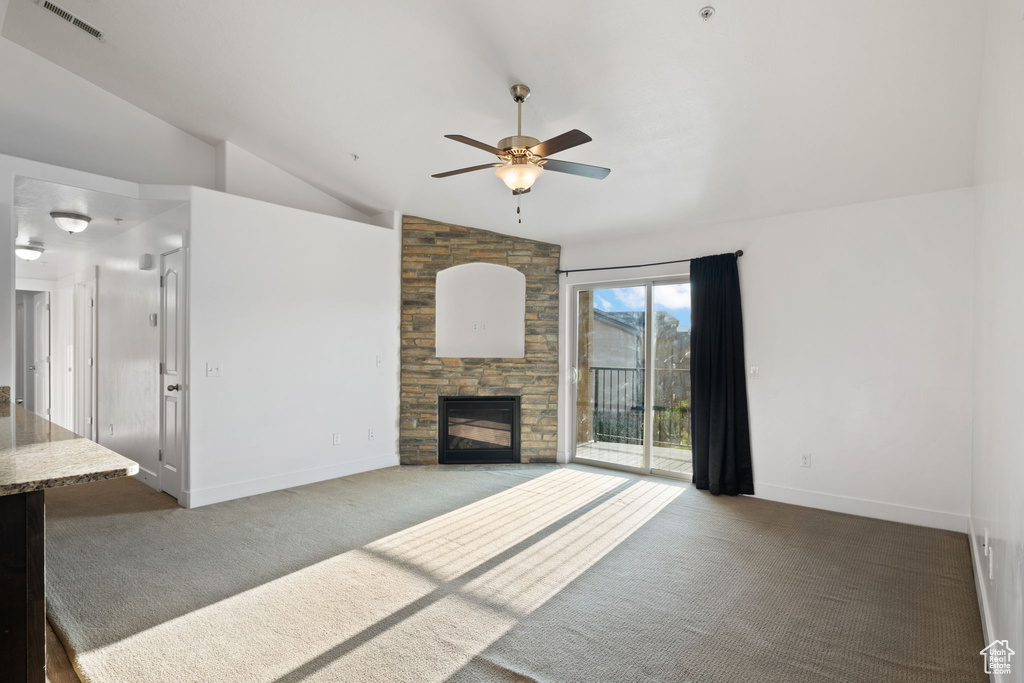 Unfurnished living room with a stone fireplace, dark colored carpet, ceiling fan, and lofted ceiling