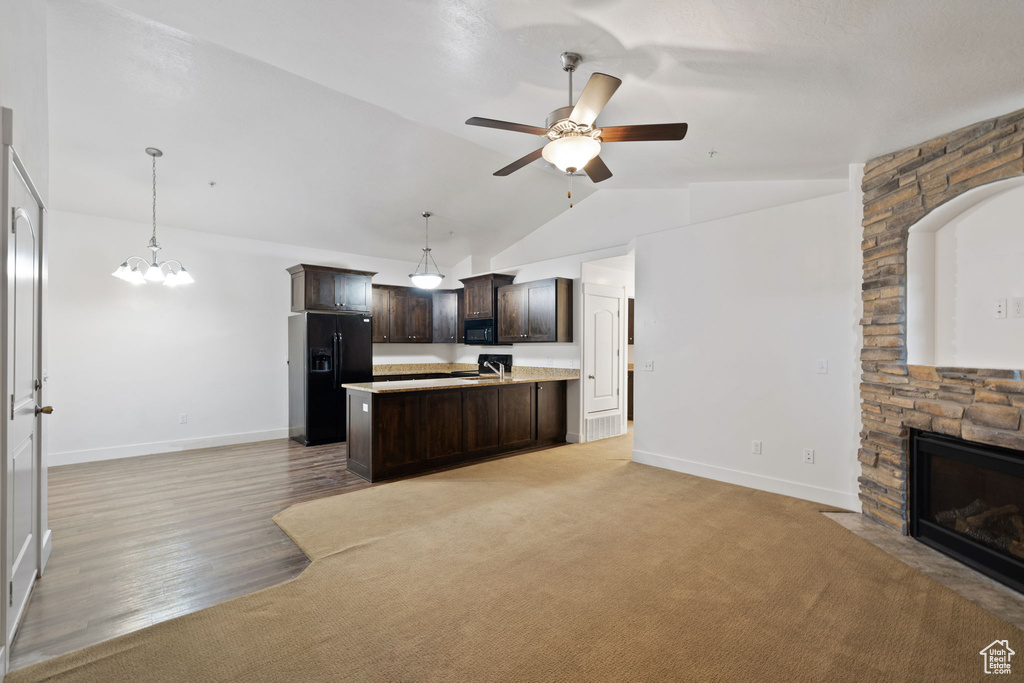 Kitchen with dark brown cabinets, ceiling fan with notable chandelier, black appliances, light colored carpet, and a stone fireplace