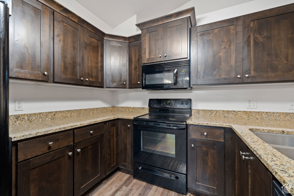 Kitchen with black appliances, dark brown cabinetry, light stone counters, and light wood-type flooring