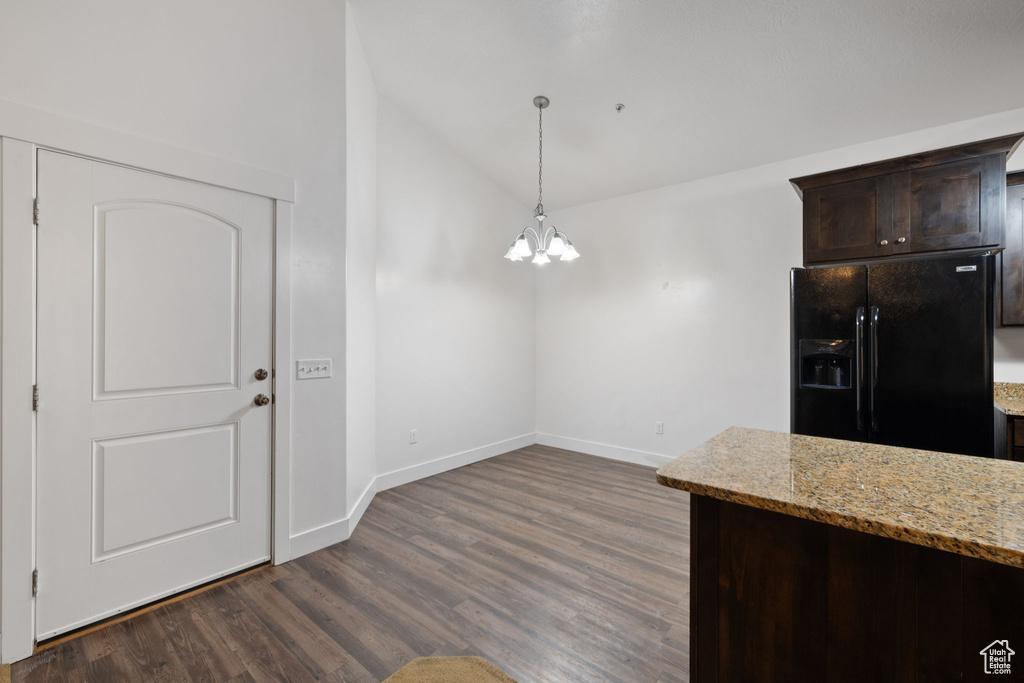 Kitchen with black fridge, light stone counters, dark brown cabinetry, and dark wood-type flooring