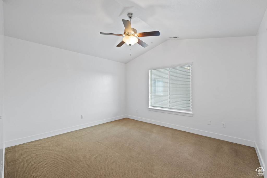 Empty room with vaulted ceiling, carpet, and ceiling fan