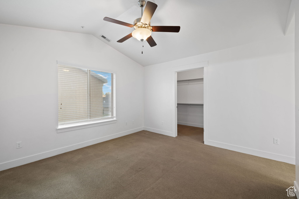 Unfurnished bedroom featuring a closet, carpet, lofted ceiling, a walk in closet, and ceiling fan