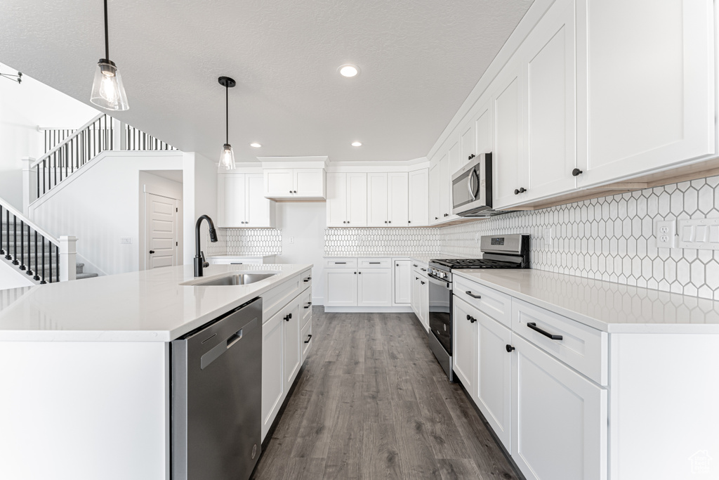Kitchen featuring sink, white cabinetry, decorative light fixtures, stainless steel appliances, and a kitchen island with sink