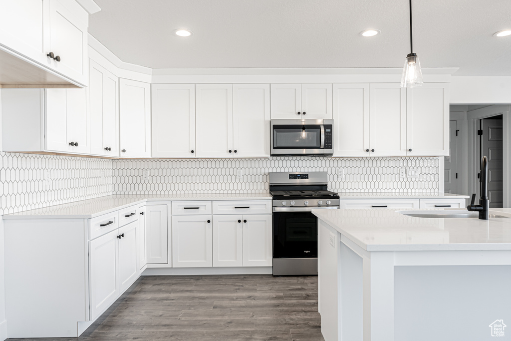 Kitchen featuring sink, hanging light fixtures, white cabinets, and stainless steel appliances