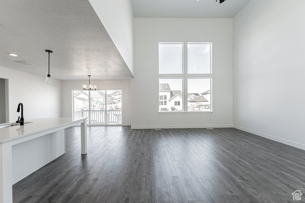 Unfurnished living room with a notable chandelier, sink, dark hardwood / wood-style floors, and a textured ceiling