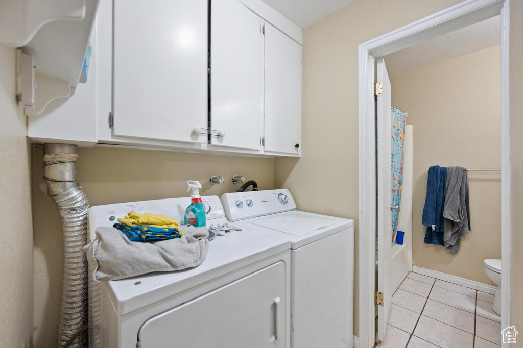 Washroom featuring washer and clothes dryer, cabinets, and light tile floors