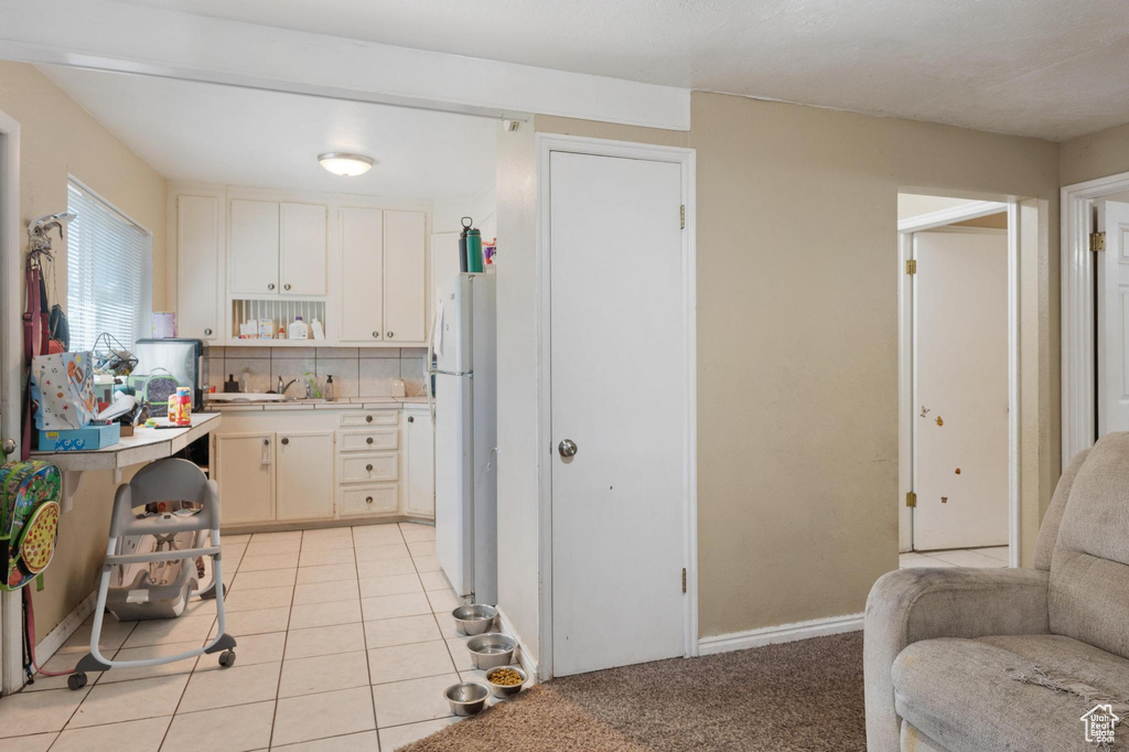 Kitchen with white refrigerator, light tile floors, white cabinetry, and backsplash