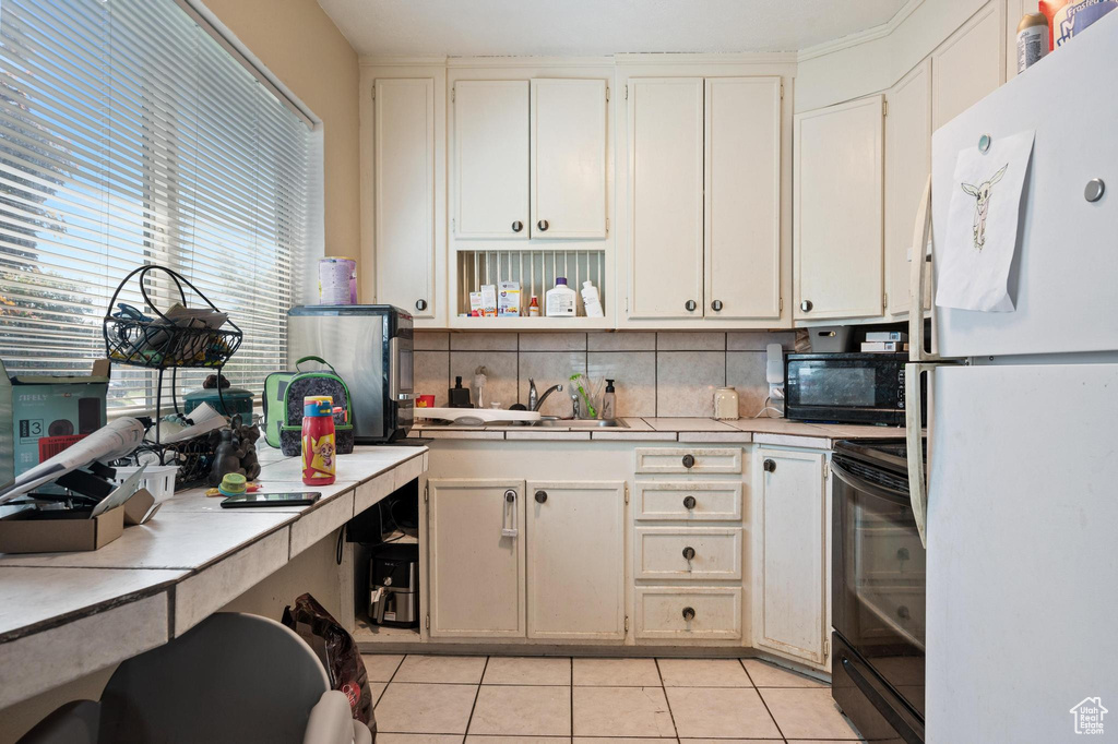 Kitchen featuring tasteful backsplash, white cabinetry, black appliances, sink, and light tile floors