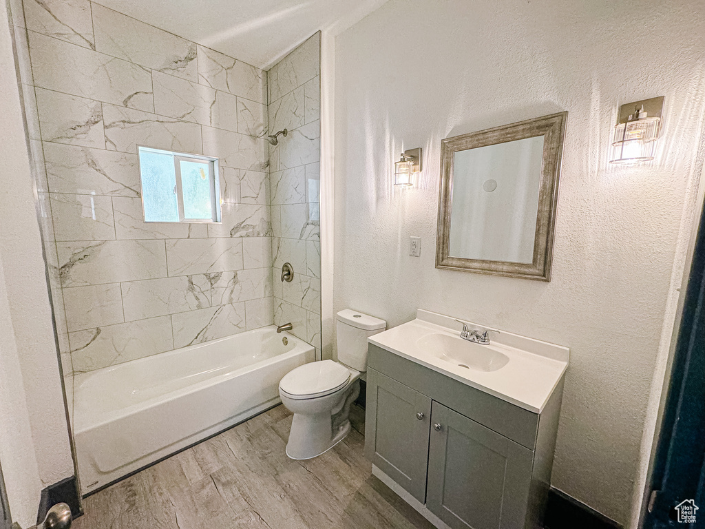 Full bathroom with vanity, toilet, tiled shower / bath, and hardwood / wood-style flooring