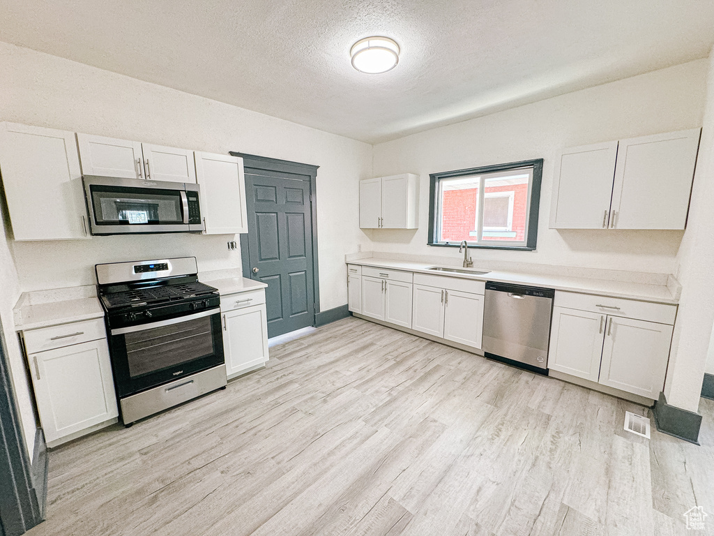 Kitchen featuring white cabinets, stainless steel appliances, light hardwood / wood-style floors, and sink