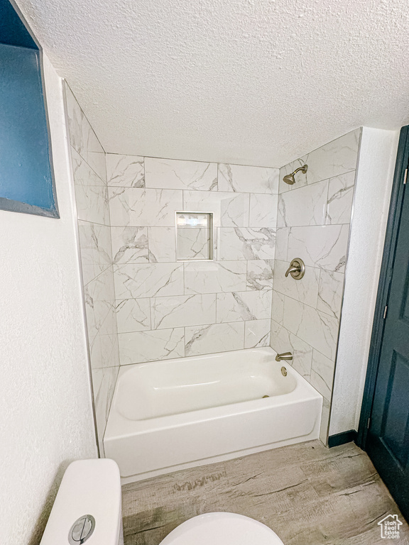 Bathroom with tiled shower / bath combo, toilet, and a textured ceiling