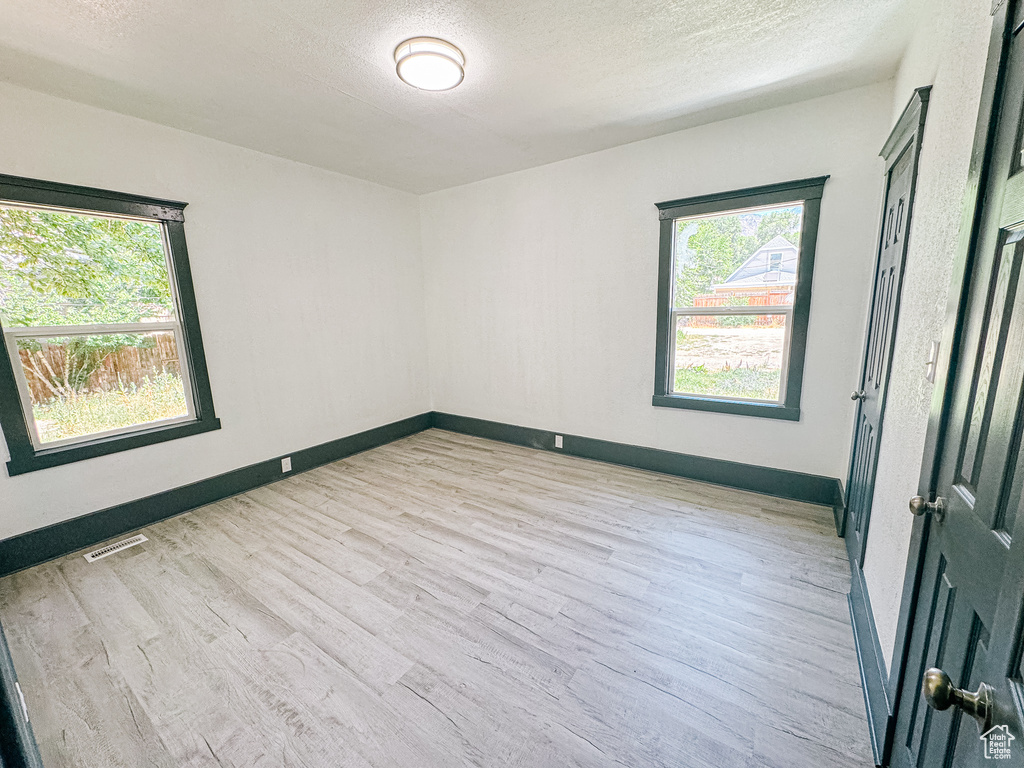 Empty room with plenty of natural light, a textured ceiling, and light hardwood / wood-style floors