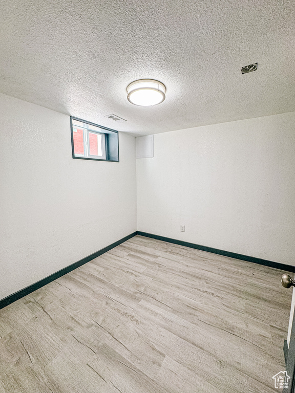 Basement featuring light wood-type flooring and a textured ceiling