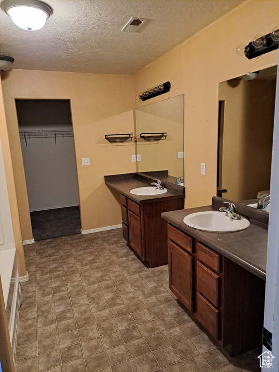 Bathroom featuring dual vanity, tile patterned flooring, and a textured ceiling