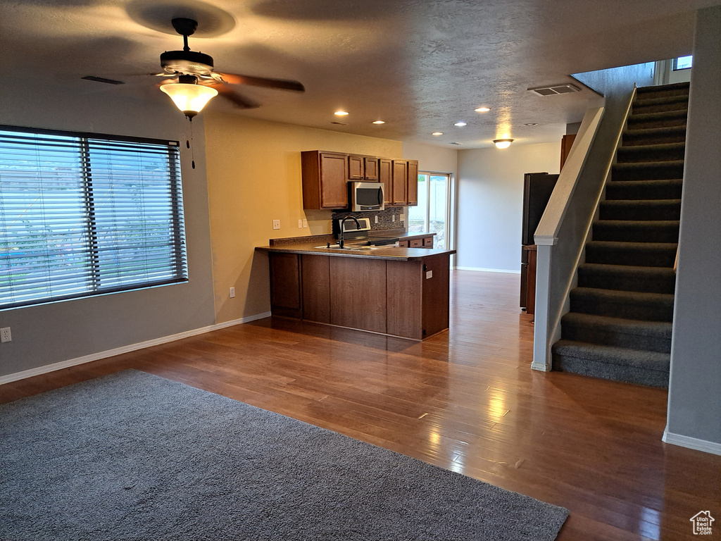 Kitchen with range with electric stovetop, kitchen peninsula, decorative backsplash, dark hardwood / wood-style flooring, and ceiling fan