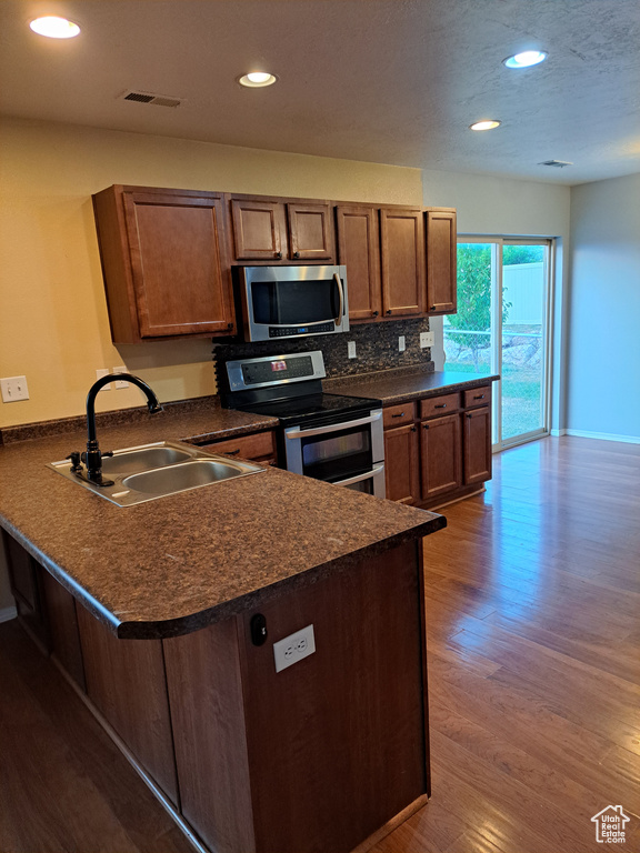 Kitchen featuring hardwood / wood-style floors, sink, a breakfast bar, appliances with stainless steel finishes, and kitchen peninsula