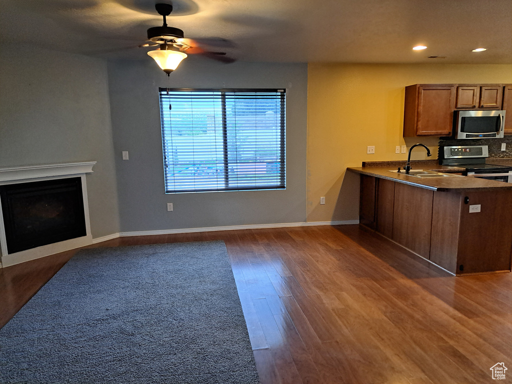 Kitchen featuring dark wood-type flooring, kitchen peninsula, appliances with stainless steel finishes, and ceiling fan