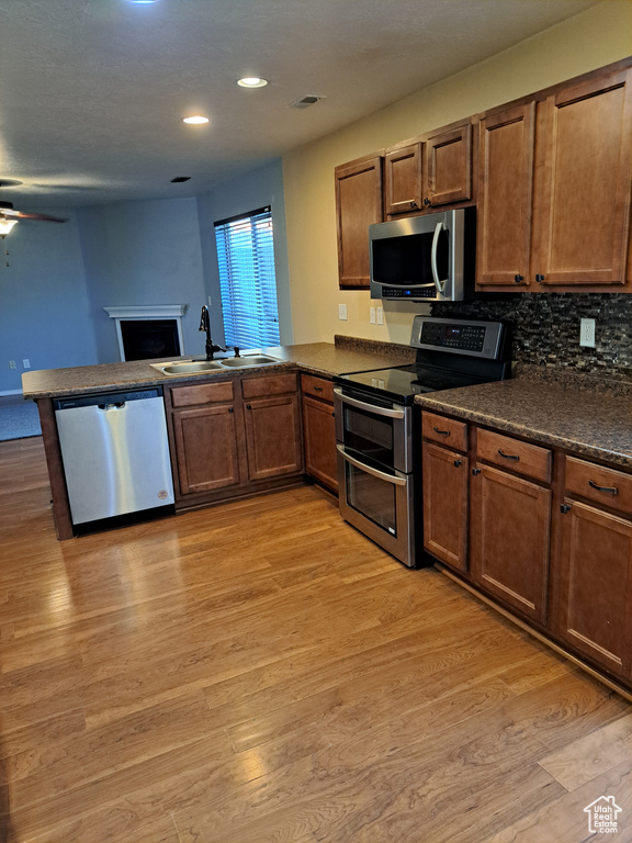 Kitchen with ceiling fan, light wood-type flooring, sink, appliances with stainless steel finishes, and kitchen peninsula