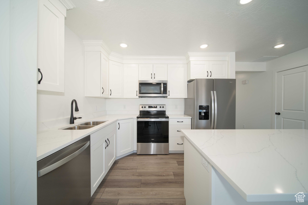 Kitchen featuring white cabinets, light stone counters, stainless steel appliances, wood-type flooring, and sink