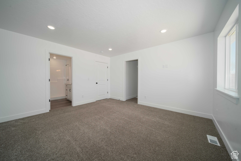 Unfurnished bedroom with carpet floors, ensuite bathroom, and multiple windows