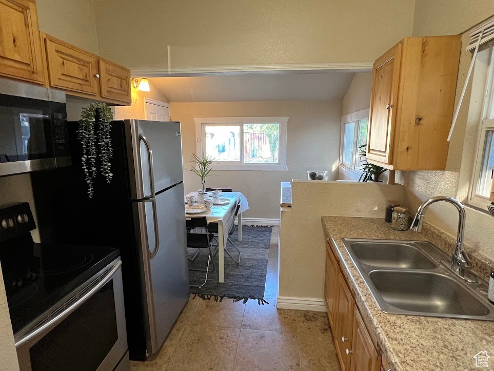 Kitchen featuring appliances with stainless steel finishes, vaulted ceiling, sink, and light tile patterned floors