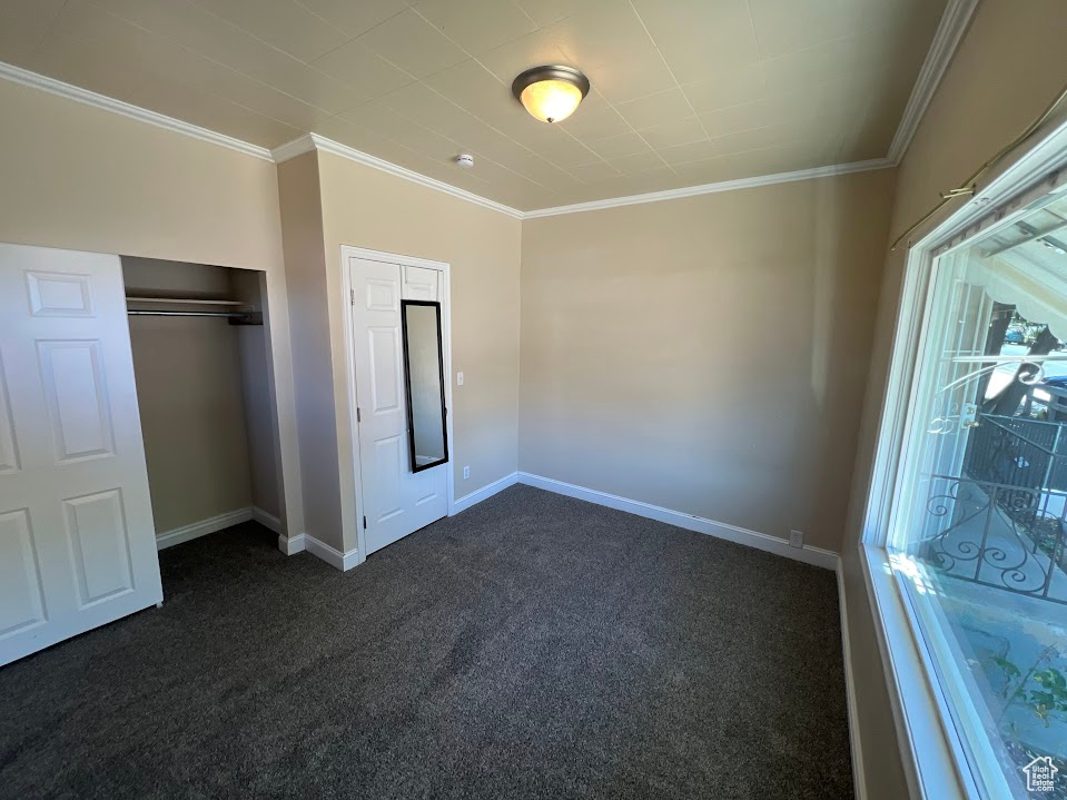 Unfurnished bedroom with dark carpet, a closet, and ornamental molding