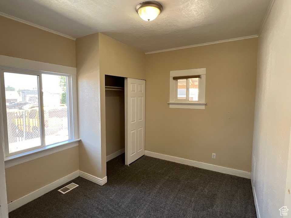 Unfurnished bedroom with ornamental molding, dark colored carpet, and a closet