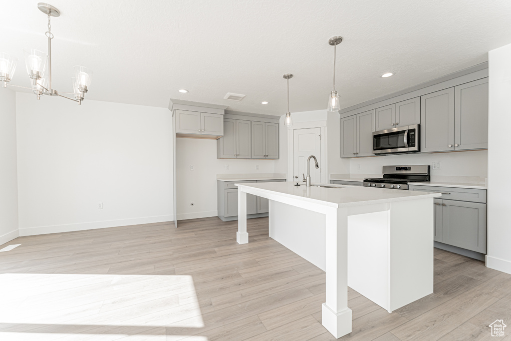 Kitchen with appliances with stainless steel finishes, sink, an island with sink, and hanging light fixtures