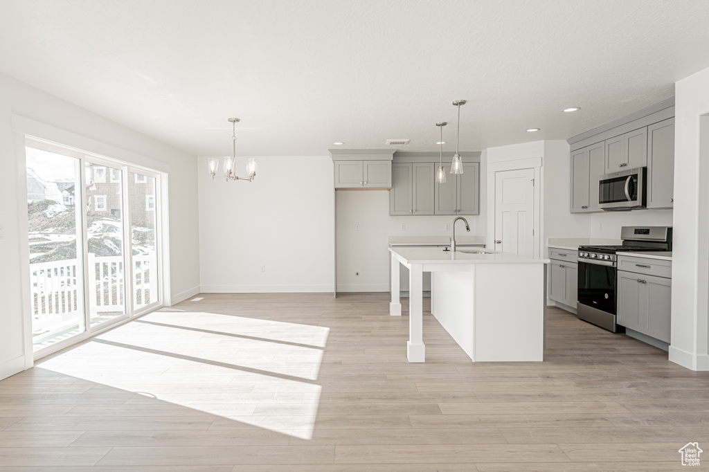 Kitchen featuring a center island with sink, appliances with stainless steel finishes, gray cabinetry, and decorative light fixtures