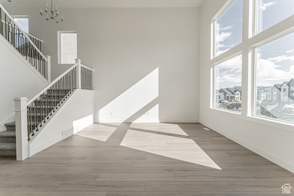Unfurnished living room featuring light hardwood / wood-style floors, an inviting chandelier, and a towering ceiling