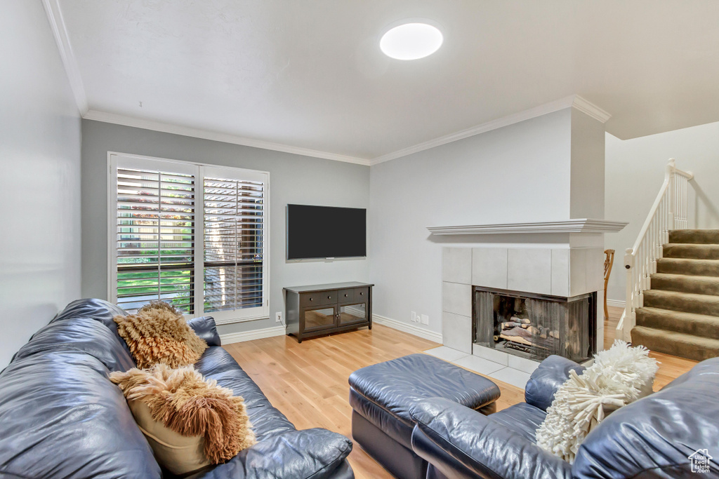 Living room with crown molding, a tiled fireplace, and light hardwood / wood-style flooring