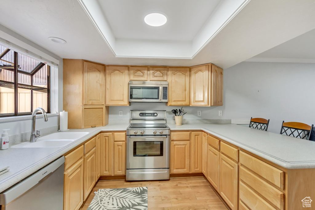 Kitchen with light brown cabinets, light wood-type flooring, kitchen peninsula, stainless steel appliances, and sink