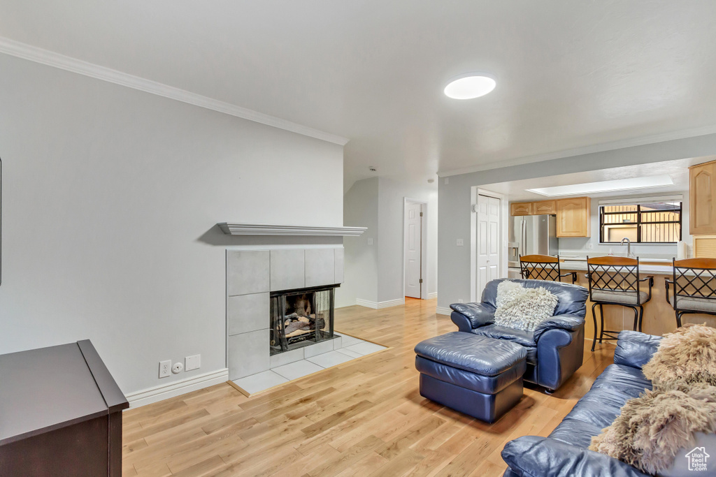 Living room with a tile fireplace, crown molding, and light hardwood / wood-style flooring