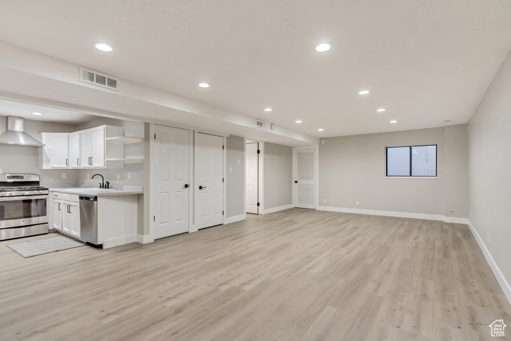 Interior space with wall chimney range hood, appliances with stainless steel finishes, light wood-type flooring, and white cabinetry