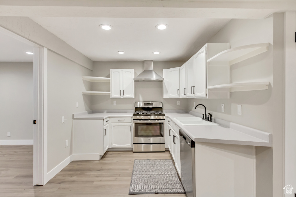 Kitchen featuring light wood-type flooring, white cabinets, stainless steel appliances, wall chimney exhaust hood, and sink