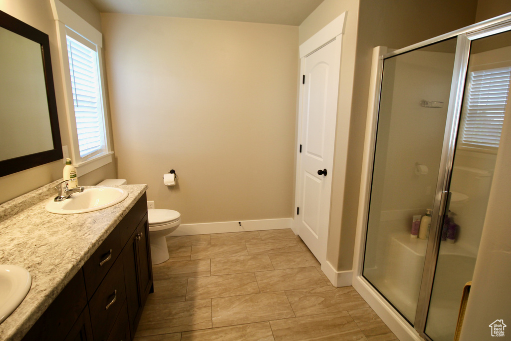 Bathroom with toilet, double sink vanity, tile patterned flooring, and an enclosed shower