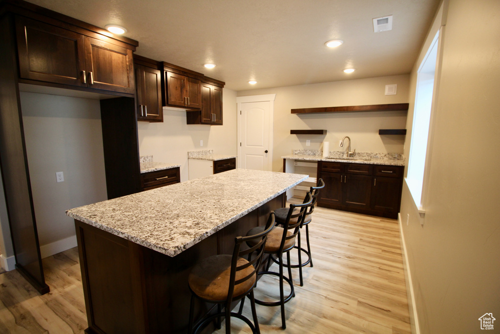 Kitchen with a center island, sink, light stone countertops, and light hardwood / wood-style floors