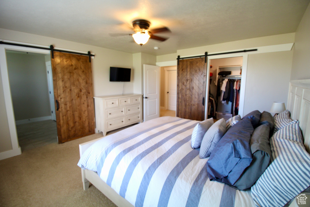 Carpeted bedroom with ceiling fan, a closet, a barn door, and a spacious closet