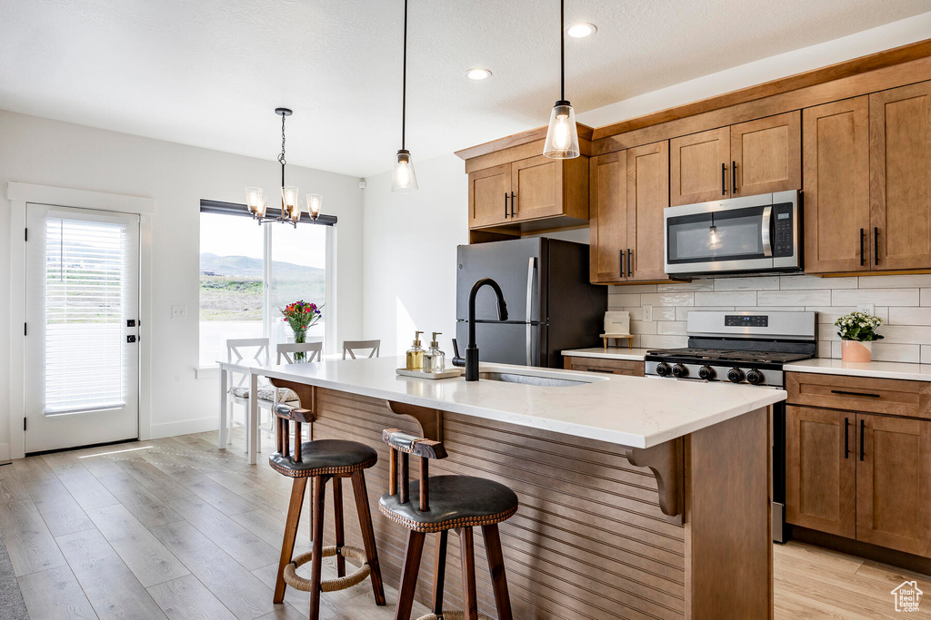 Kitchen featuring stainless steel appliances, backsplash, light hardwood / wood-style flooring, a kitchen breakfast bar, and a kitchen island with sink