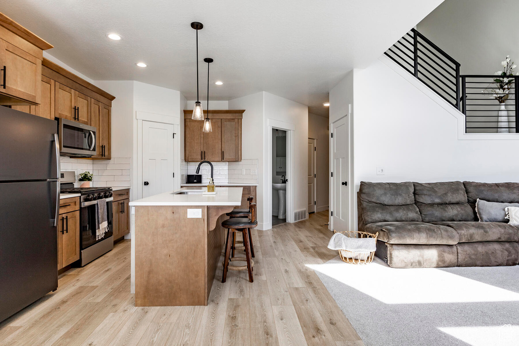 Kitchen featuring stainless steel appliances, a center island with sink, sink, backsplash, and light wood-type flooring