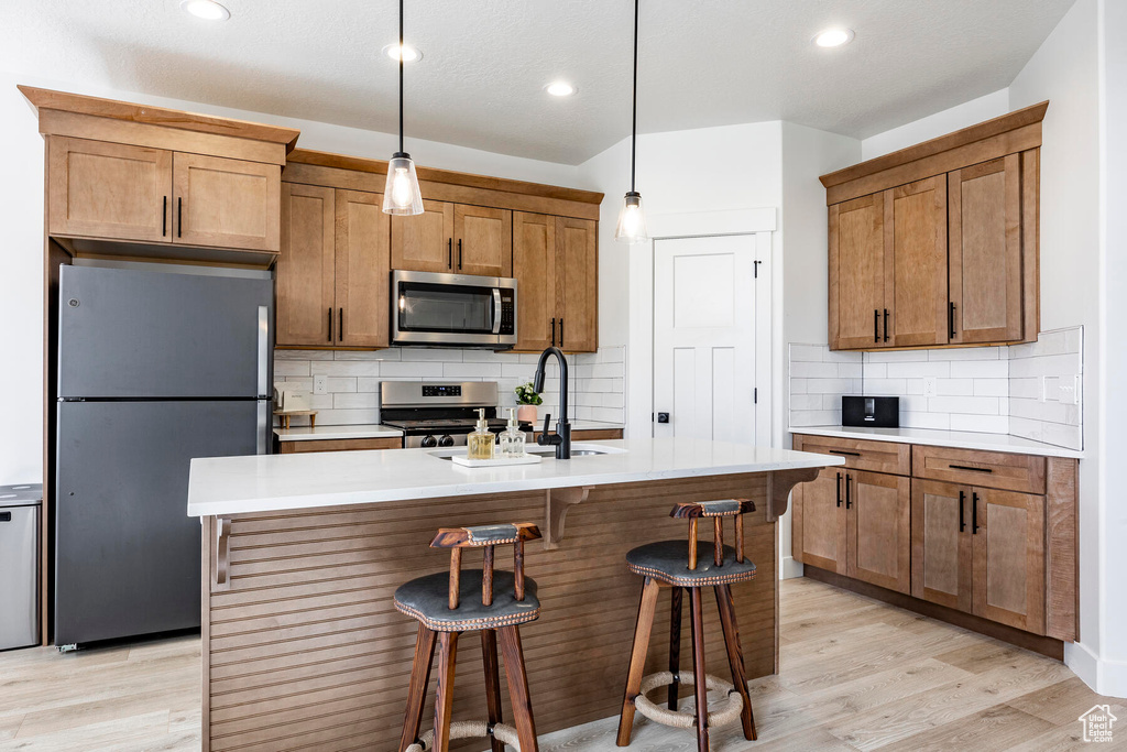 Kitchen with decorative backsplash, light wood-type flooring, stainless steel appliances, and an island with sink