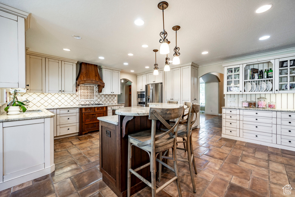 Kitchen with a kitchen breakfast bar, appliances with stainless steel finishes, custom exhaust hood, decorative backsplash, and hanging light fixtures